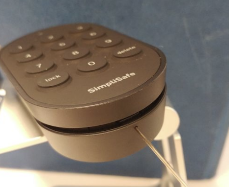 The PIN Pad for the Smart Lock with a paperclip being placed in the hole to open the top of it.